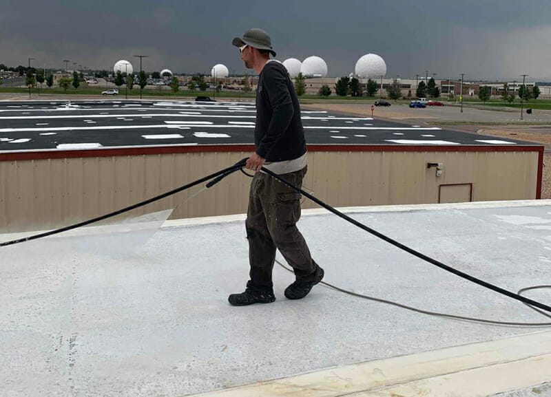 Roofing contractor applying a roof coating on a commercial roof in Colorado Rockies